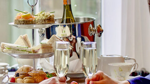 Afternoon tea with champagne and assorted pastries by a window at a charming hotel.