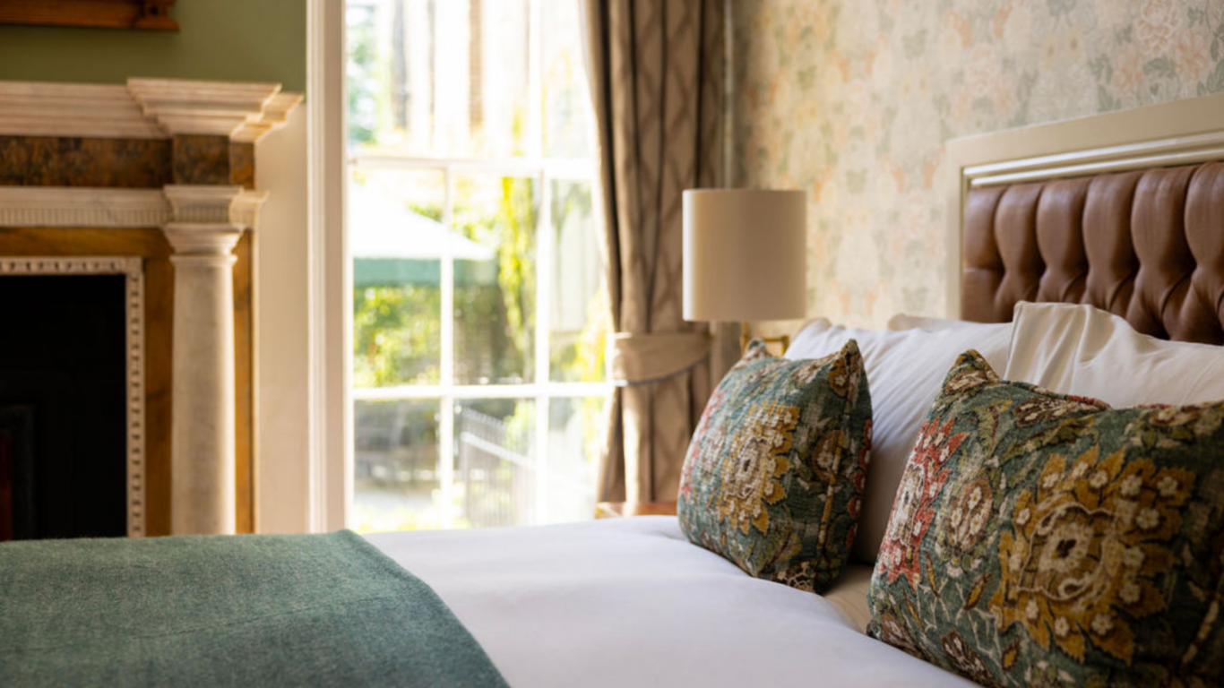 Inviting hotel room with plush bed, elegant cushions, large window, and picturesque garden view, perfect for relaxation.
