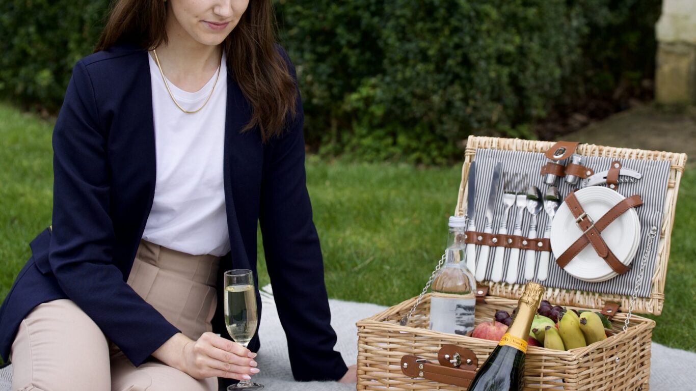 Woman enjoying a luxury picnic with champagne and pastries on a hotel lawn, surrounded by lush greenery.